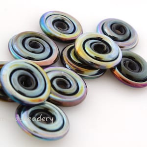 May include: A group of iridescent black glass beads with a spiral design. The beads have a metallic sheen and are arranged in a pile.