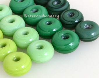 May include: A set of 14 green glass beads, ranging in colour from light green to dark green. The beads are round and have a smooth, glossy finish.