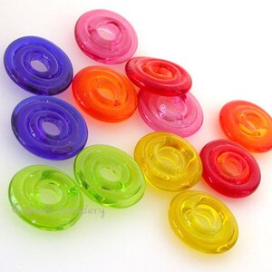 K&ouml;nnte beinhalten: Sortiment aus bunten runden Glaskn&ouml;pfen mit einem Loch in der Mitte. Die Kn&ouml;pfe sind in den Farben Rot, Orange, Gelb, Gr&uuml;n, Blau und Lila.