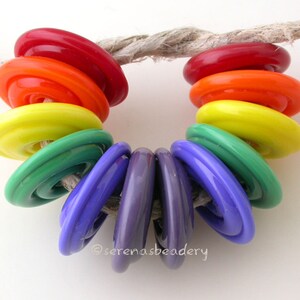 K&ouml;nnte beinhalten: Ein Regenbogen aus bunten Glasperlen, die auf einem St&uuml;ck Schnur aufgef&auml;delt sind. Die Perlen sind in der Reihenfolge der Farben des Regenbogens angeordnet, beginnend mit Rot und endend mit Lila.