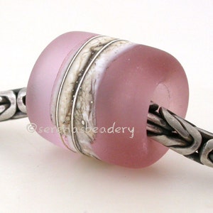 May include: A pink glass bead with white and brown stripes. The bead is on a silver chain.