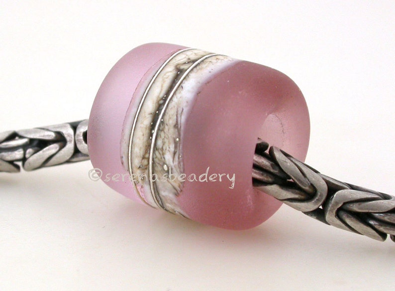 May include: A pink glass bead with white and brown stripes. The bead is on a silver chain.