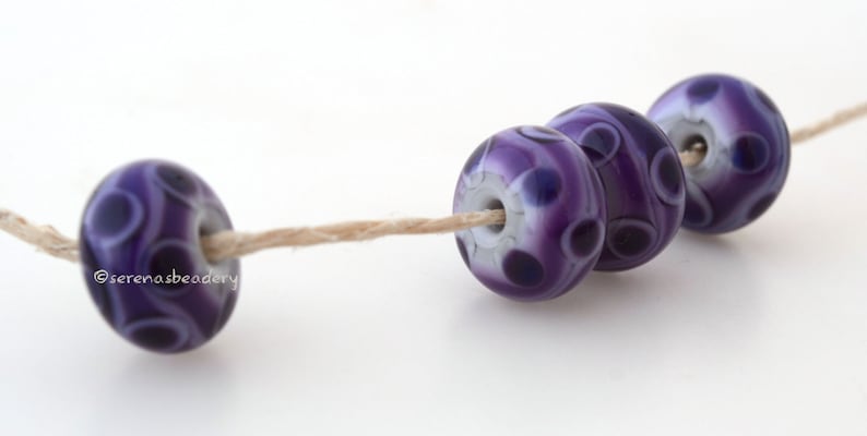 May include: Four purple and white glass beads with a swirling pattern are strung on a natural twine thread. The beads are round and have a glossy finish.