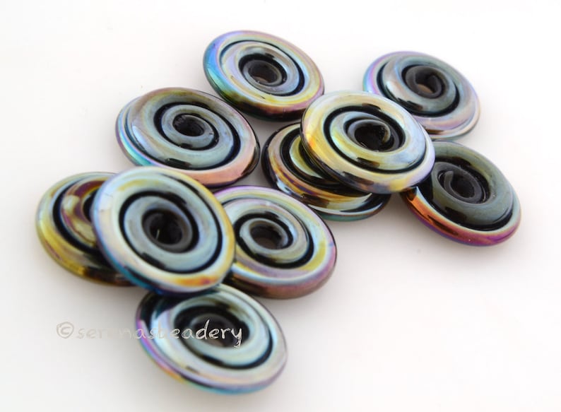 May include: A group of iridescent black glass beads with a spiral design. The beads have a metallic sheen and are arranged in a pile.