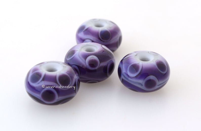 May include: Four purple and white glass beads with a swirl pattern. The beads have a hole in the center for stringing.