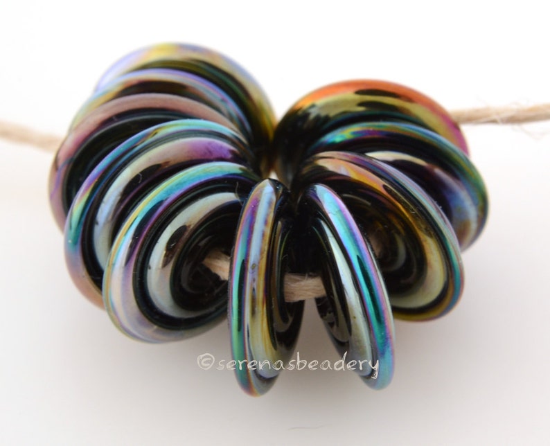 May include: A stack of iridescent black glass beads with a rainbow sheen. The beads are arranged in a spiral shape.