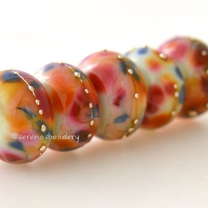 May include: A string of five colorful glass beads with a white background and gold accents. The beads are a mix of red, orange, yellow, and blue.