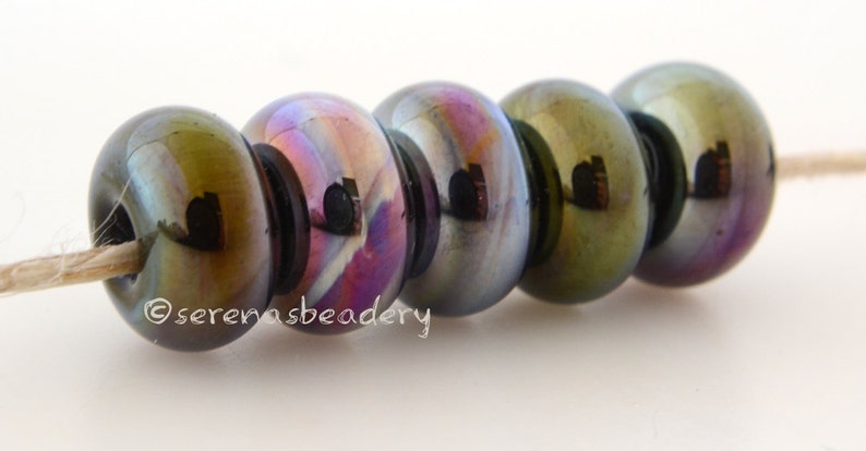 May include: Five iridescent glass beads with a dark green, blue, and purple color shift. The beads are strung on a white thread.