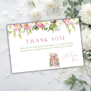 May include: A white thank you card with pink flowers and green leaves around the top. The text "THANK YOU" is in pink. The text "Thank you for making my bridal shower so wonderful! Your presence, love, and generosity are deeply appreciated!" is in black. The text "with love, Ava" is in pink. There is a drawing of a stack of books with a pink ribbon and flowers on top.