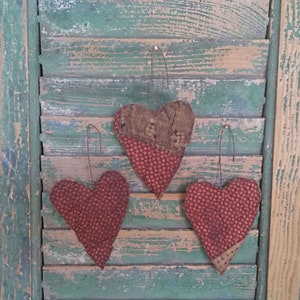 3 heart ornaments made from grunged and stiffened antique quilt. Each ornament has a rusty wire hanger.