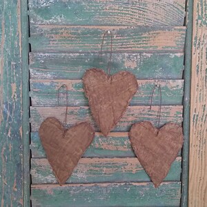 This image shows the back side of 3 small heart-shaped ornaments made from grunged and stiffened antique quilt. Each ornament has a rusty wire hanger.