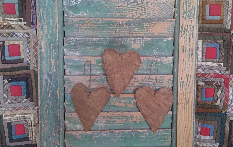 This image shows the back side of 3 small heart-shaped ornaments made from grunged and stiffened antique quilt. Each ornament has a rusty wire hanger.