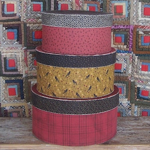 May include: A stack of four round decorative boxes. The boxes are covered in various patterned fabrics, including floral, plaid, and bird designs. The colors include red, black, and yellow. The boxes are of varying sizes, with the largest at the bottom.