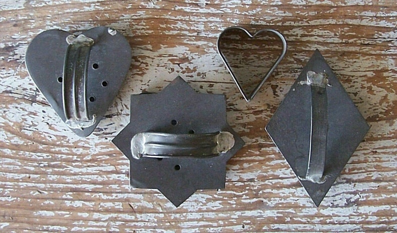 Close-up of the back side of 4 antique or very vintage cookie cutters with soldered handles.