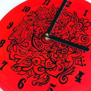 May include: A red vinyl record clock with black numbers and a black and white abstract design. The clock hands are black.