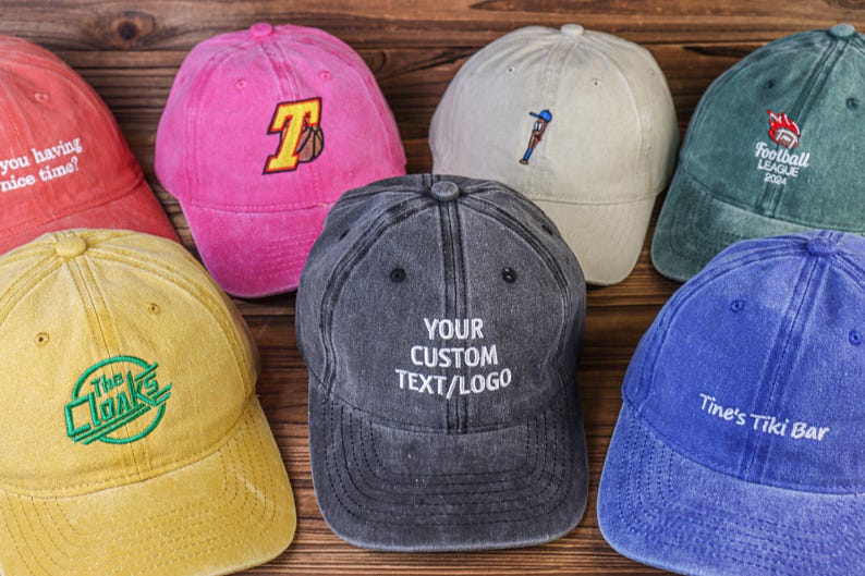 May include: A collection of ten vintage-style baseball caps in various colors, including pink, beige, green, blue, and yellow. Each cap features a different embroidered design, including a basketball, a baseball player, a football, a band logo, and the text "Your Custom Text/Logo".