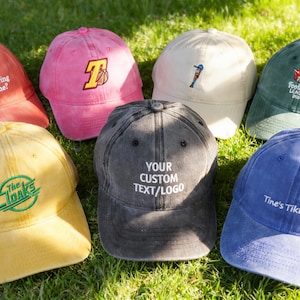 May include: A selection of baseball caps in shades of red, pink, yellow, grey, green, and blue. Each cap displays embroidered text or logos, including "you having nice time?", "The Cloaks", and "Tine's Tiki Bar".