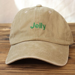 May include: A tan baseball cap with a green embroidered word "Jelly" on the front.