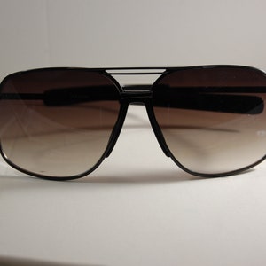 May include: Black aviator sunglasses with brown gradient lenses. The sunglasses have a double bridge and a metal frame.