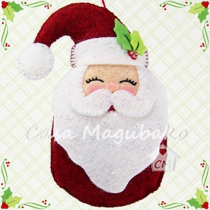 May include: Red felt Santa Claus ornament with a white beard and a white pom-pom on his hat. The ornament has a green felt holly leaf on top of his hat.