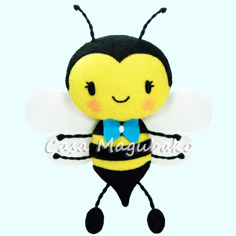 Pu&ograve; includere: Un giocattolo di ape in feltro con strisce nere e gialle, ali bianche e un papillon blu. L'ape ha un viso sorridente con occhi neri e guance rosa.