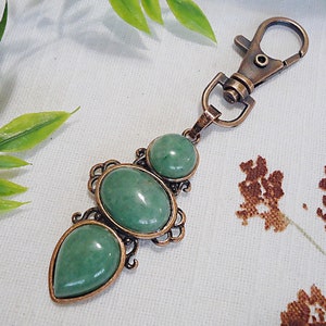 May include: A copper-toned key chain with three green gemstone charms. The charms are oval and teardrop shaped and are set in ornate metalwork.
