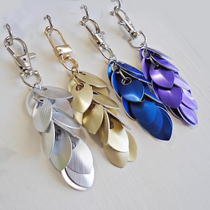 May include: Three silver keychains with a chainmail design. The keychains are silver, gold, and purple.