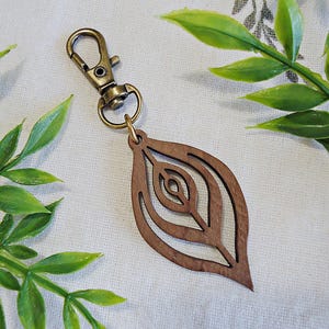 May include: A wooden leaf-shaped keychain with a brass clasp. The leaf has a detailed, intricate design with multiple layers.