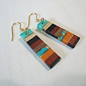 May include: A pair of colorful wood and resin earrings with gold hooks. The earrings are rectangular and feature turquoise, orange, brown, and black stripes.