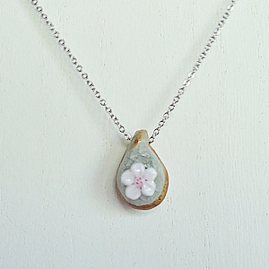 May include: A silver chain necklace with a teardrop-shaped pendant. The pendant is light green with a white flower with a pink center.