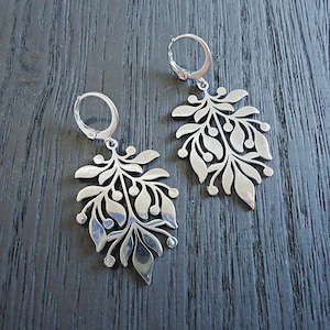 May include: A pair of silver earrings with a delicate, leafy design. The earrings are made of metal and have a dangling, floral shape.