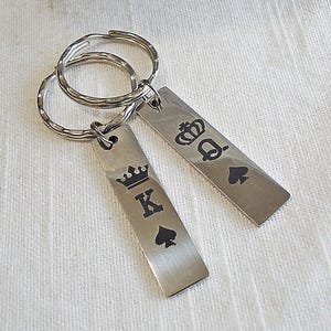 May include: A pair of silver keychains with a black spade and crown design. One keychain says "K" and the other says "Q".