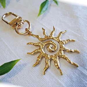 May include: Gold-toned metal sun keychain with a spiral design. The sun has a textured surface and is attached to a gold-toned metal swivel clasp.