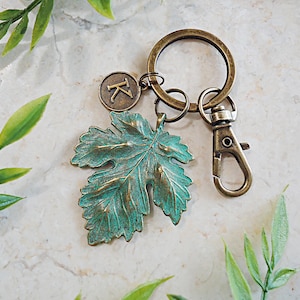 May include: A teal green leaf charm with a bronze finish attached to a bronze key chain with a letter K charm.