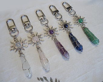 May include: Five silver keychains with a sun design and a crystal point pendant. The crystals are clear, pink, purple, blue, and green.