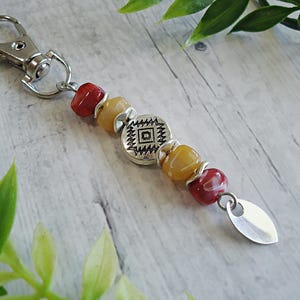 May include: A beaded keychain with a silver clasp and a decorative charm. The keychain features red, yellow, and silver beads, along with a silver charm with a geometric design. The charm is approximately 1 inch long.