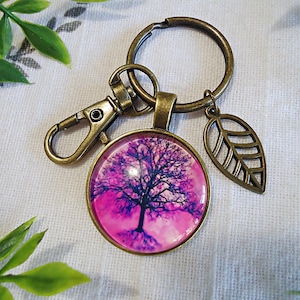 May include: A bronze key chain with a pink and purple tree charm, a bronze leaf charm, and a bronze clasp.