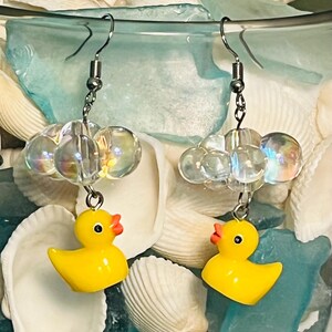 May include: A pair of yellow rubber ducky earrings with clear iridescent beads hanging from silver hooks.