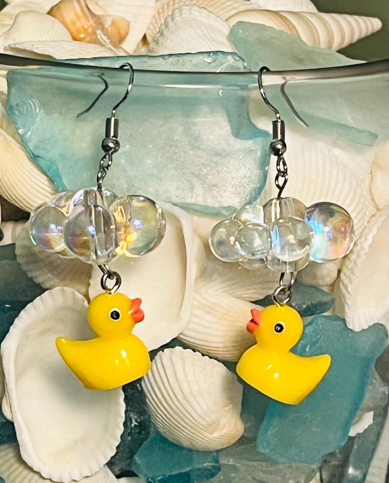 May include: A pair of yellow rubber ducky earrings with clear iridescent beads hanging from silver hooks.