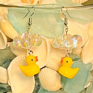 May include: A pair of yellow rubber ducky earrings with iridescent clear beads. The earrings are hanging from silver hooks.