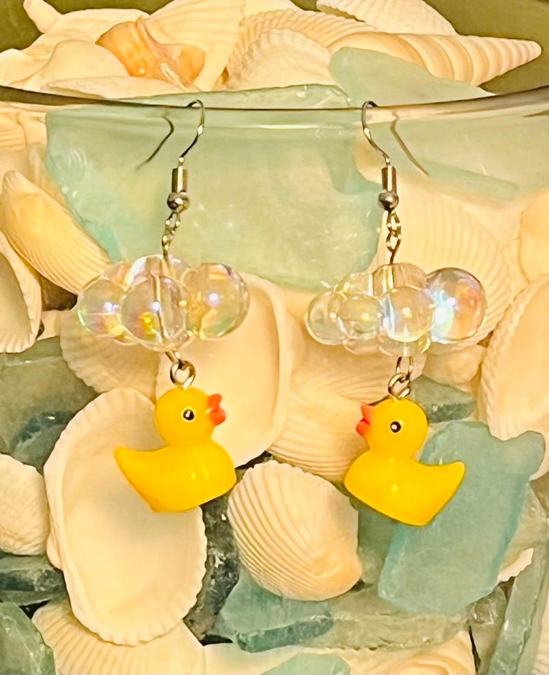 May include: A pair of yellow rubber ducky earrings with iridescent clear beads. The earrings are hanging from silver hooks.