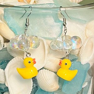 May include: A pair of yellow rubber ducky earrings with iridescent clear bead clouds hanging from silver hooks.