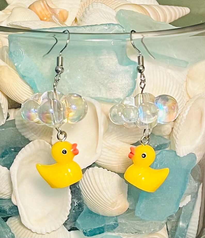 May include: A pair of yellow rubber ducky earrings with iridescent clear bead clouds hanging from silver hooks.