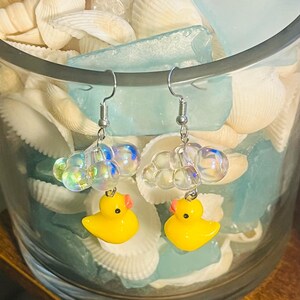 May include: A pair of silver earrings with a yellow rubber ducky charm and iridescent bubble beads.