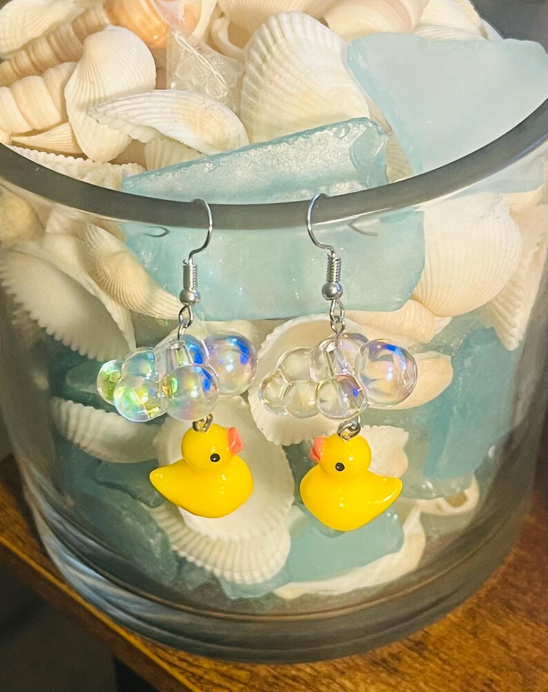May include: A pair of silver earrings with a yellow rubber ducky charm and iridescent bubble beads.