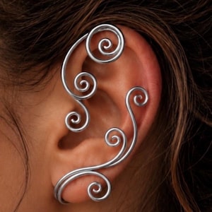May include: A silver-toned ear cuff featuring a series of interconnected wire spirals that follow the outer curve of the ear. The metal design consists of multiple circular coils of varying sizes, creating a continuous, flowing pattern along the cartilage.
