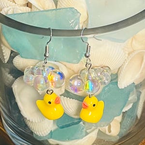 May include: A pair of yellow rubber ducky earrings with iridescent glass beads. The earrings are hanging from silver hooks.