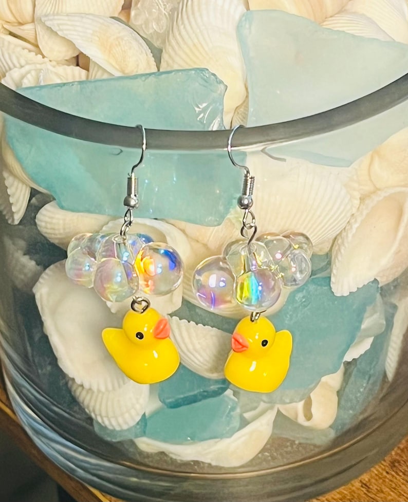 May include: A pair of yellow rubber ducky earrings with iridescent glass beads. The earrings are hanging from silver hooks.