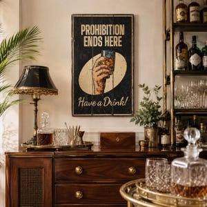 May include: A rectangular wall sign with a black background featuring the text PROHIBITION ENDS HERE and Have a Drink! in cream-colored lettering. The center displays a graphic of a hand holding a glass of amber liquid inside a cream oval.