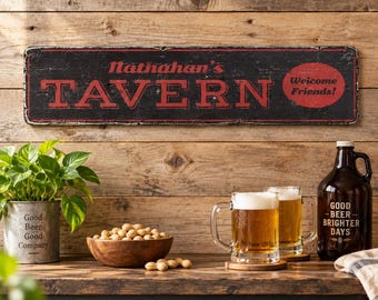 Può includere: Un'insegna rettangolare nera con bordi usurati presenta la scritta rossa "Nathanan's TAVERN" e un cerchio rosso contenente le parole "Welcome Friends!". Sotto, una ciotola di legno con arachidi si trova accanto a due boccali di birra e un boccione.